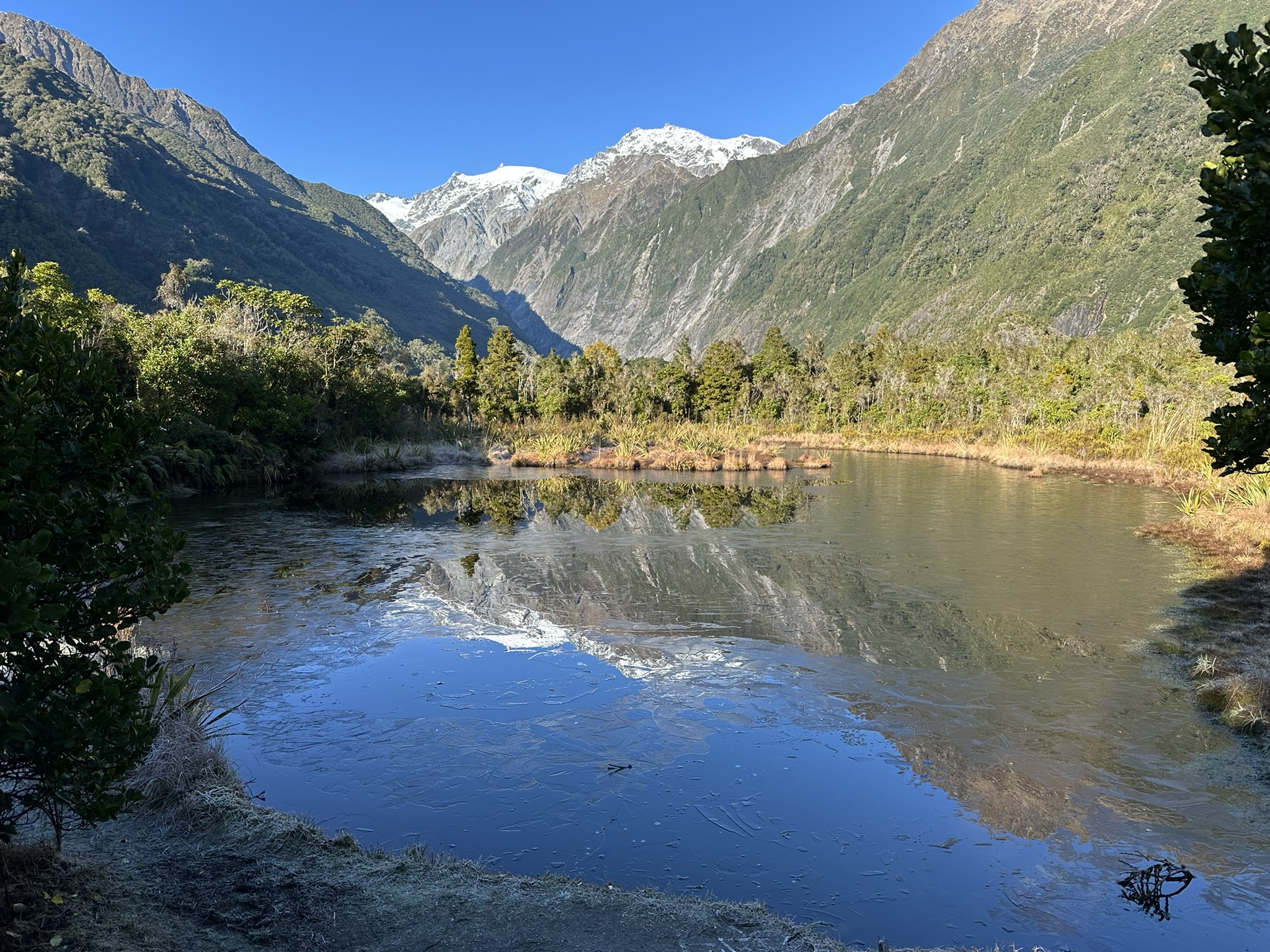 A scenic mountain landscape reflecting in a pool of water and ice.